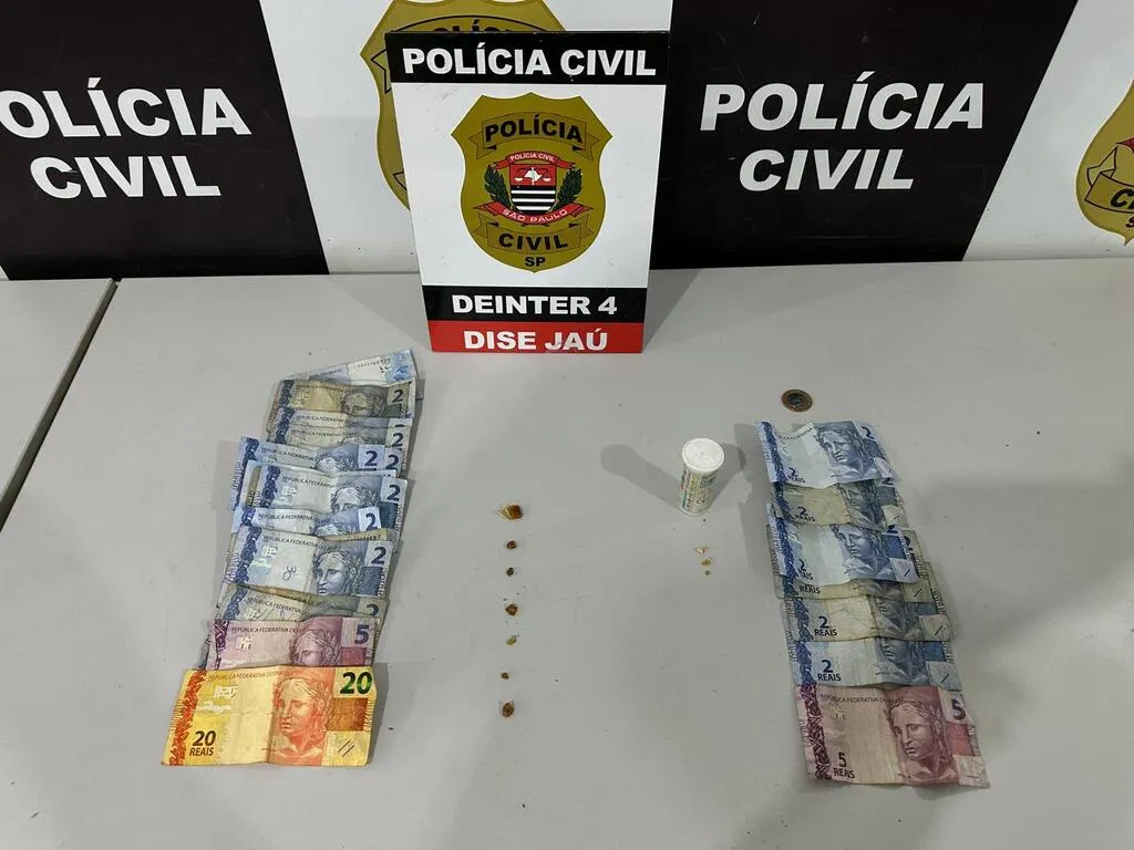 Dinheiro e porções de entorpecente em cima de uma mesa, com painel da Polícia Civil ao fundo