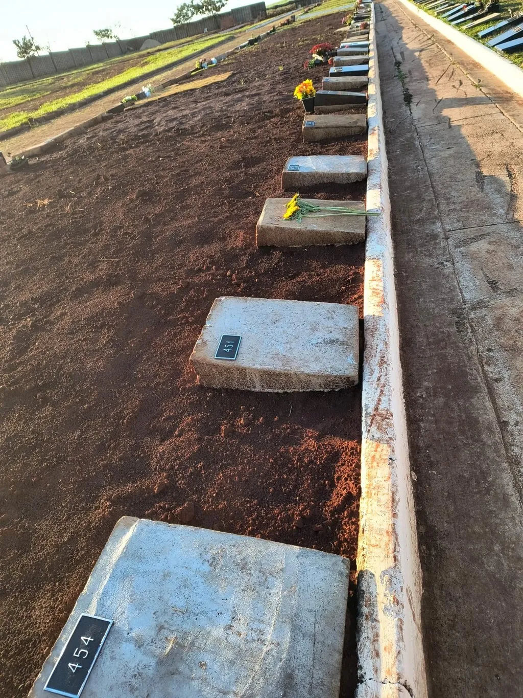 Terreno com sepulturas em concreto, identificadas com placas numéricas, tendo do lado direito calçada em concreto com guia na cor branca
