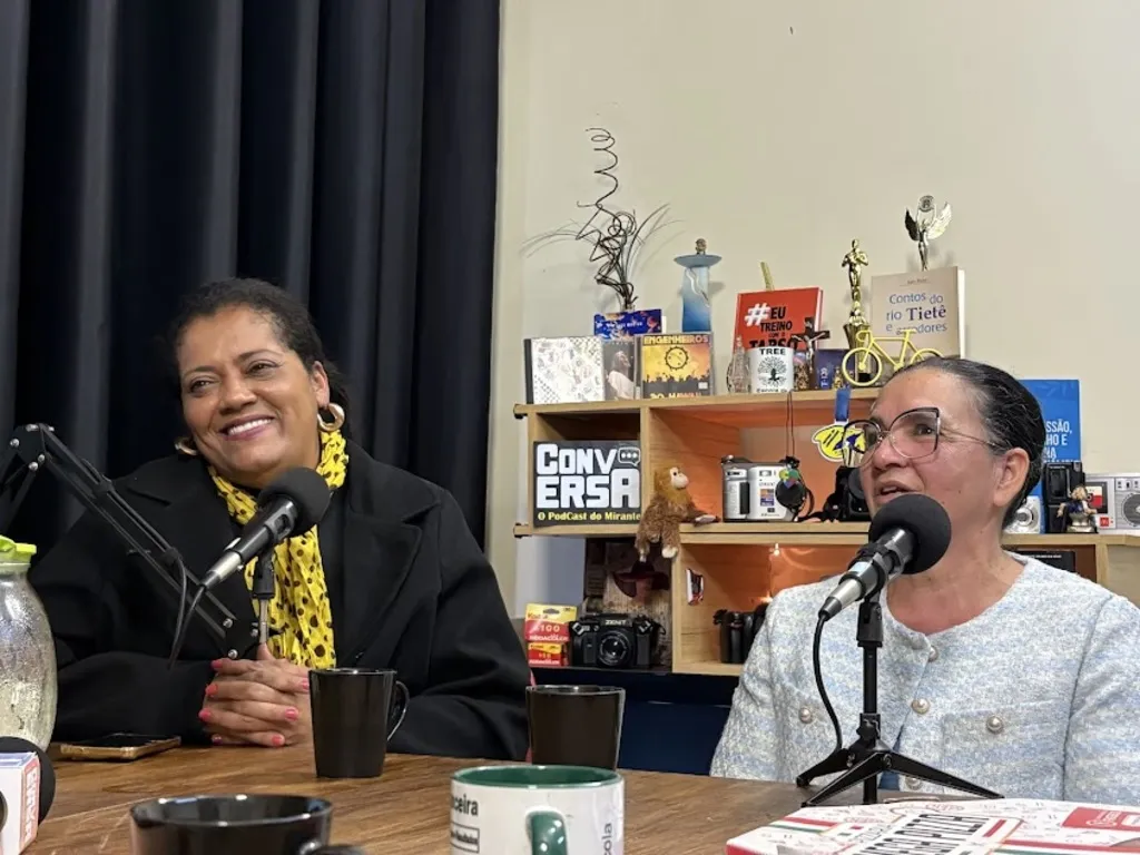 duas mulheres sentadas à mesa de um podcast