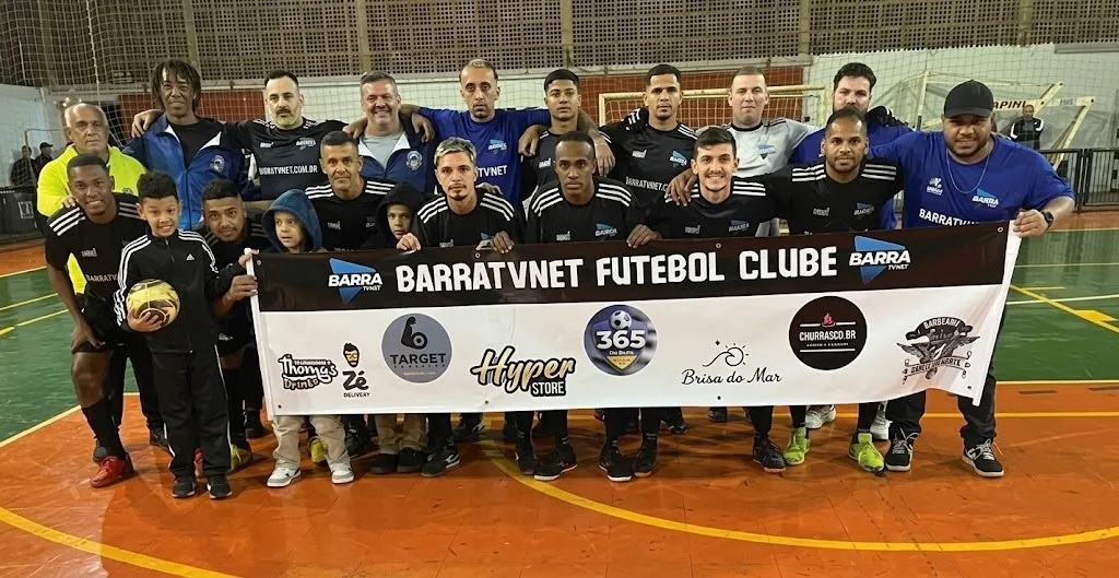 equipe de atletas com uniforme preto e azul posam atrás de faixa com patrocinadores