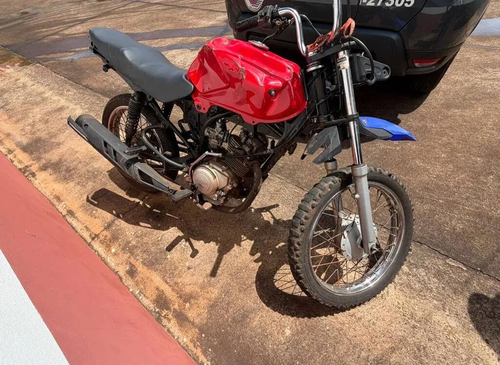 Motocicleta vermelha com tanque amassado, faltando várias peças estacionada em um local ao ar livre
