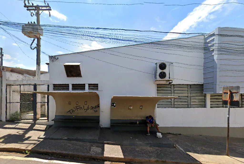 Ponto de ônibus com duas coberturas de concreto e bancos, com um homem sentado de cabeça baixa na direita