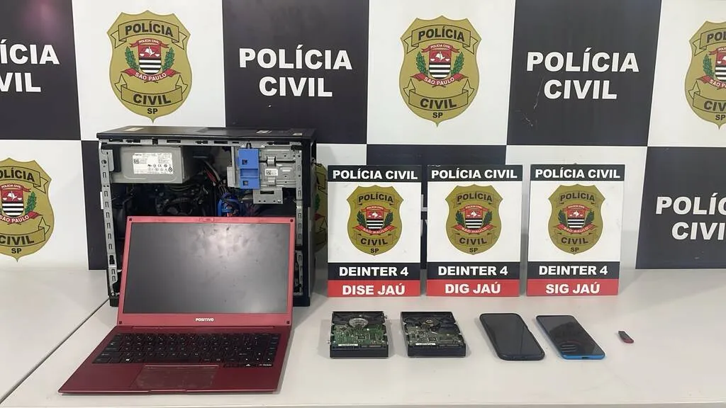 Computadores, telefones celulares e peças de informática colocados a frente de um painel com o símbolo da Polícia Civil de São Paulo