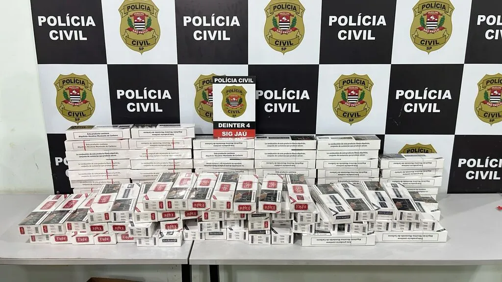 Pacotes de cigarro em uma mesa, com painel da Polícia Civil do Estado de São Paulo ao Fundo