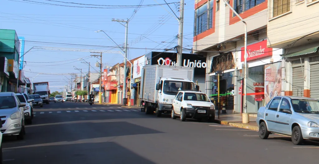 Rua com pessoas caminhando na calçada e carros estacionados
