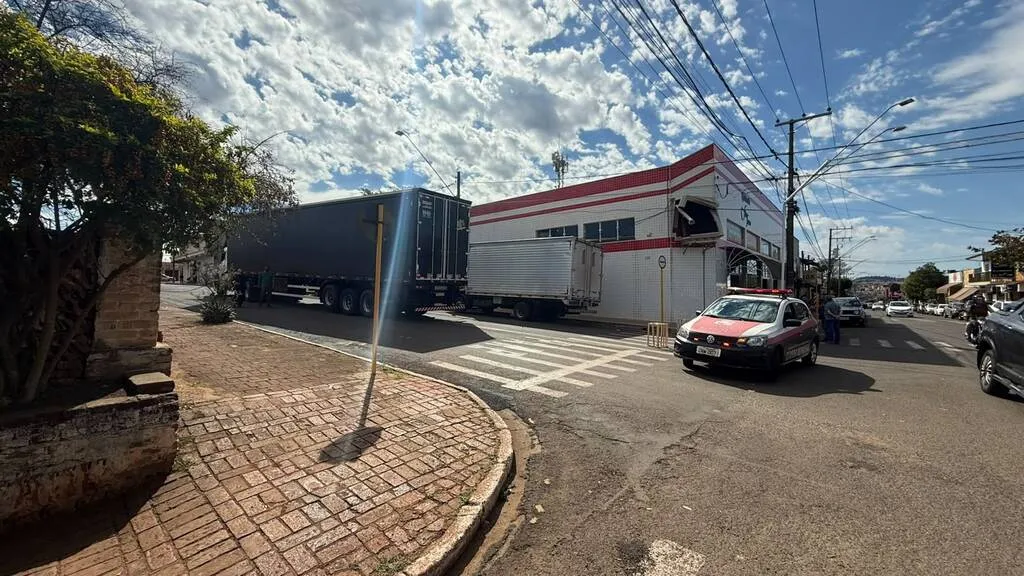 cruzamento de ruas com caminhão grande e alto parado, e uma fachada com equipamento de ar condicionado destruído; fios caídos dos postes