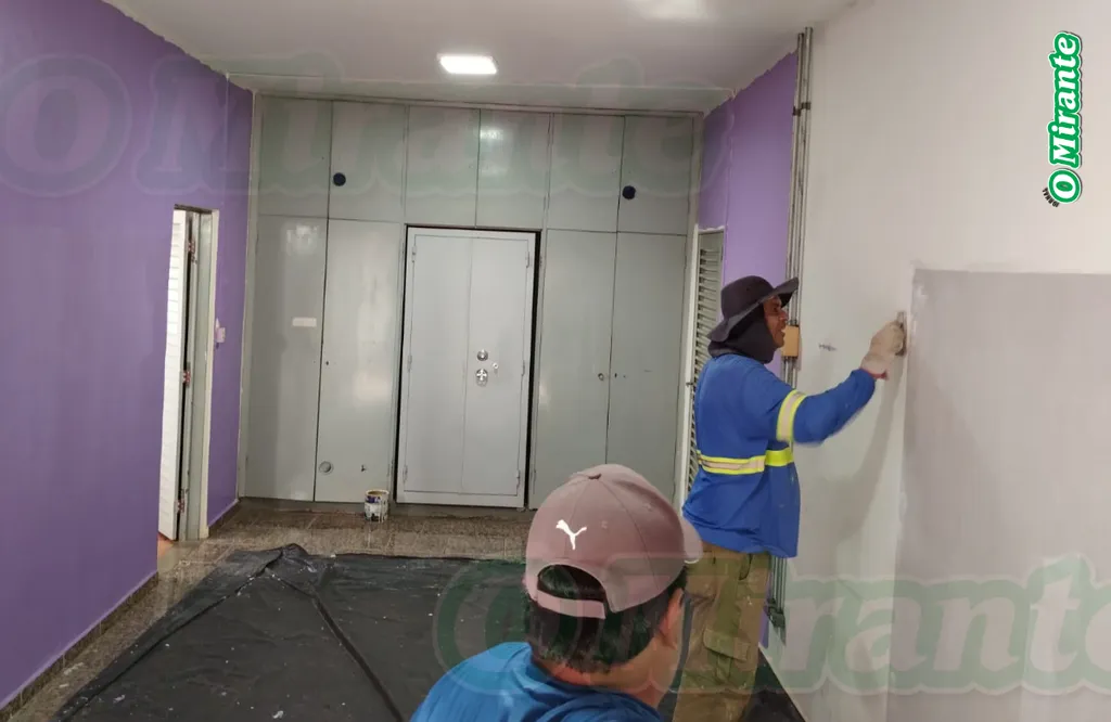 dois homens pintam uma parede de lilás em sala com armários ao fundo