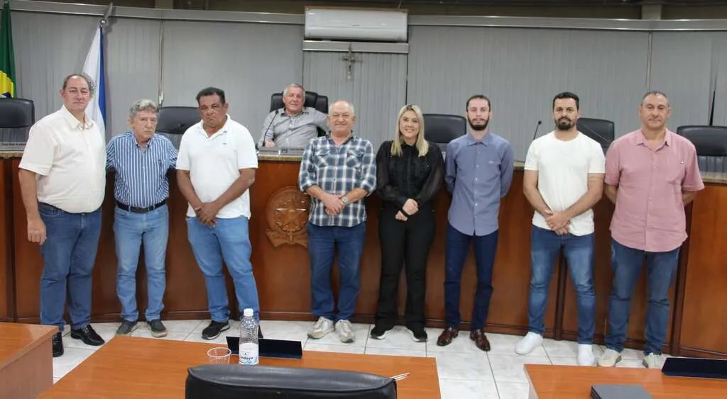 Plenário da Câmara Municipal, com oito pessoas em pé à frente, e uma sentada ao fundo, atrás de uma mesa