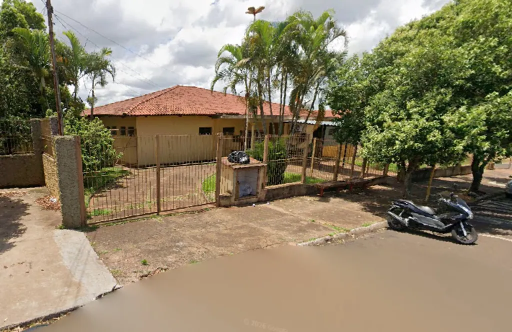 Prédio na cor amarela, com grade frontal, árvores e uma motocicleta estacionada
